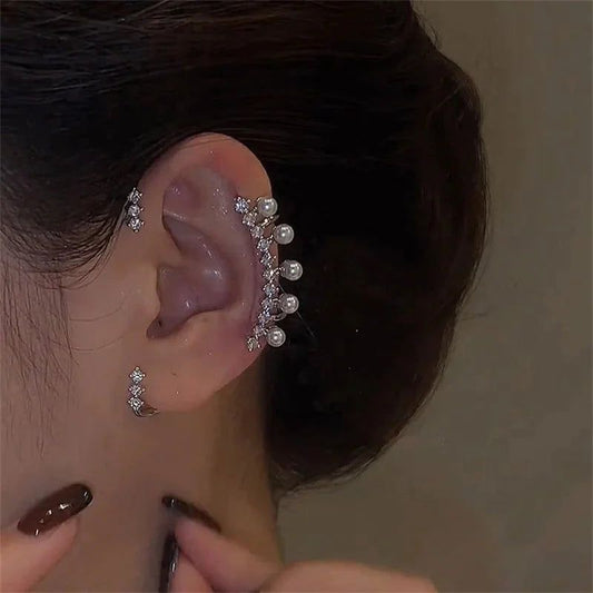 A close-up of a woman's ear wearing the Miccelli Luxe Silver Color Pearl Ear Cuff—Vintage Crystal Zircon Ear Clip (no piercing required)—with small pearls on the cartilage, her dark hair pulled back, and her hand touching her neck.